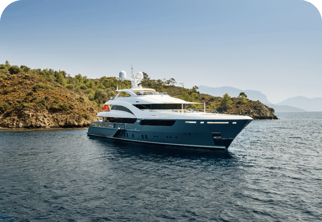 Luxurious yacht sailing near a rocky coastline with lush greenery under a clear blue sky.